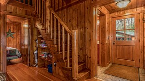 A wooden staircase leading to a second floor, a wooden door with a window, and a small bookshelf with books.