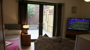 A room with a bed, a sofa, a television displaying a tennis match, and a sliding glass door leading to an outdoor area. - The Nook - Farm Park Stay with Hot Tub, BBQ & Fire Pit (Swansea)