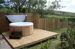 Un jacuzzi en una terraza de madera con vistas a un campo cubierto de hierba y árboles.