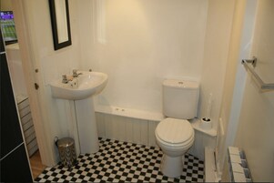 A bathroom with a white sink, toilet, and bathtub. The floor has a black and white checkered pattern.