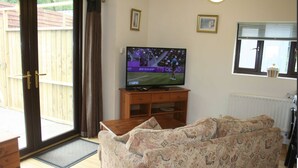 A living room with a television, sofa, wooden cabinet, and a window with blinds. - The Nook - Farm Park Stay with Hot Tub, BBQ & Fire Pit (Swansea)