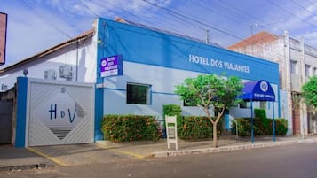 Um hotel chamado 'Hotel dos Viajantes' com fachada azul, entrada protegida por portão e uma placa.