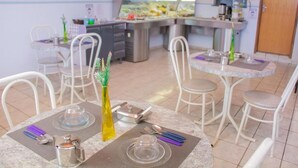 Comedor con mesas redondas, sillas blancas y un mostrador de buffet al fondo.