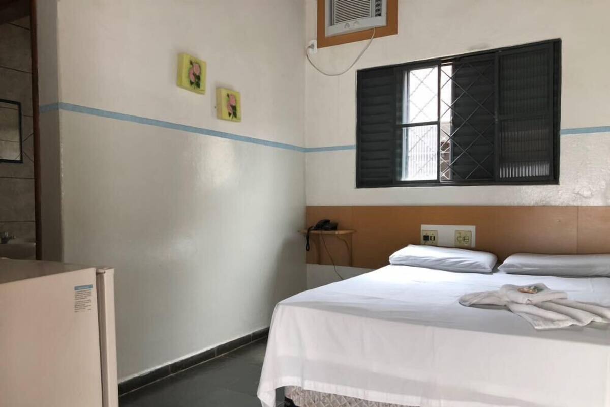 Une chambre d’hôtel avec un lit, une table de chevet avec un téléphone et une fenêtre avec des volets.