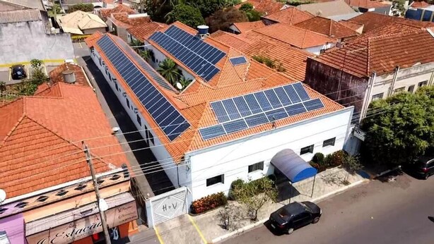 Un edificio con varios paneles solares en el techo, una zona de estacionamiento y un pequeño jardín.