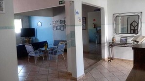 Un vestíbulo de hotel con una zona de estar, un televisor, cuadros enmarcados en las paredes y un espejo sobre un pedestal.