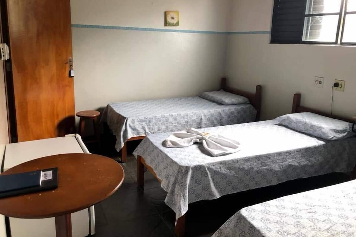 Une petite pièce simple, avec deux lits simples, une porte en bois, une petite table et une fenêtre.