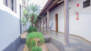 Un patio estrecho con un pequeño jardín, un corredor cubierto y un edificio con extintor en la pared.