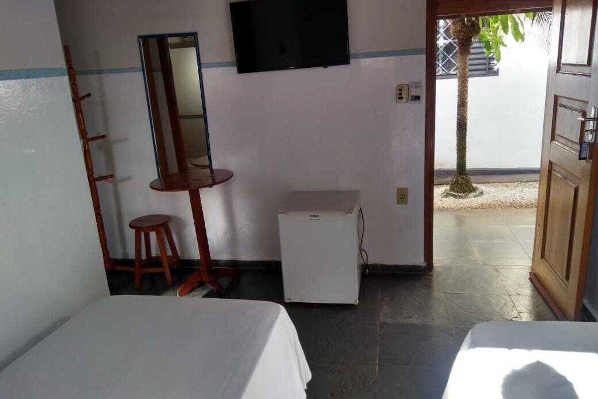 Une chambre d’hôtel avec deux lits, une petite table, un miroir, une télévision et un réfrigérateur.