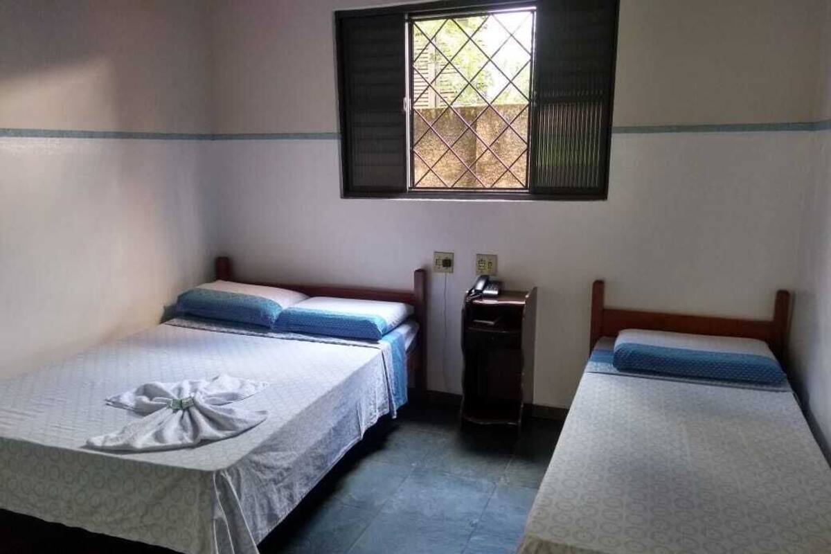 Une chambre avec deux lits, une petite table et une fenêtre avec des barreaux.
