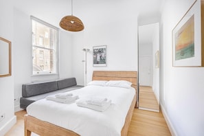 Cozy retreat with a large bed, grey bench, and pendant light, set against a minimalist backdrop.