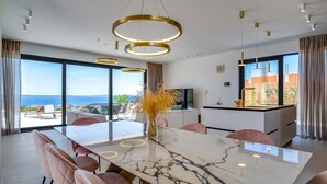 Zona pranzo moderna con tavolo in marmo, sedie rosa e vista sul mare.