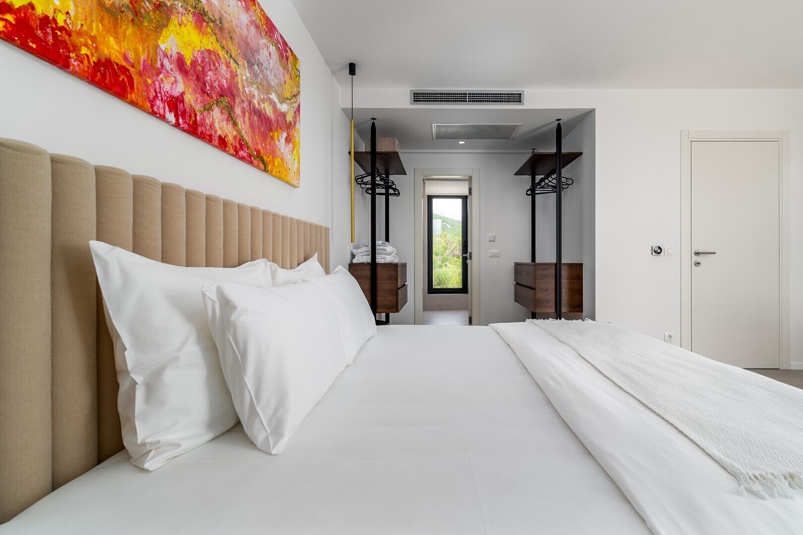 Une chambre moderne avec un grand lit, une tête de lit, un tableau et une vue sur un balcon.