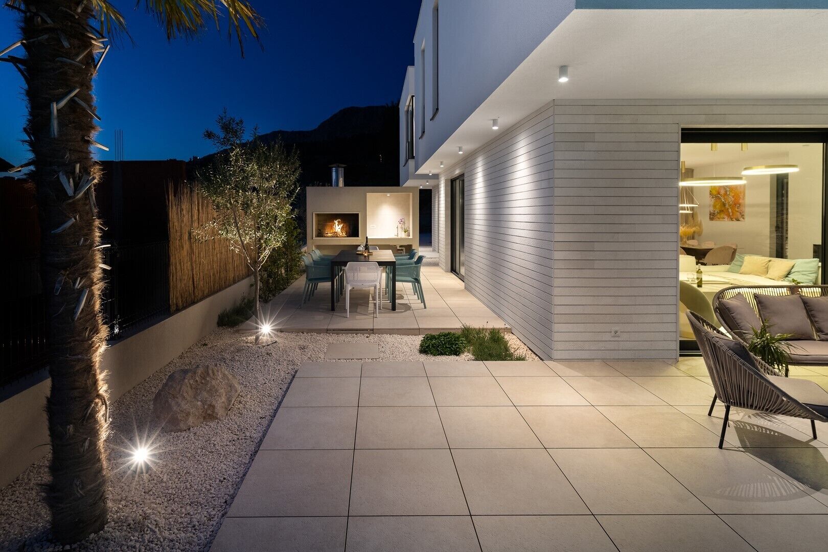 Une terrasse extérieure moderne comprenant un espace repas, un foyer et un coin salon confortable avec des coussins.