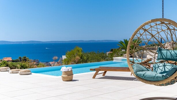 Area piscina con una sedia a dondolo, poltrone relax e vista sul mare.