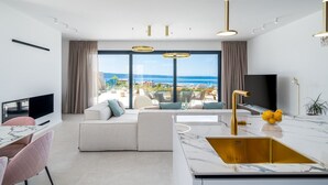 Un soggiorno moderno con una grande finestra, un divano, un'area pranzo e una cucina con un piano di lavoro in marmo.