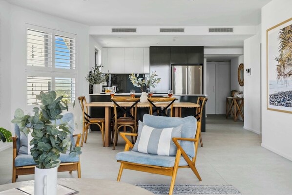 A modern kitchen with a central island, dining area with chairs, and a living space with a sofa.