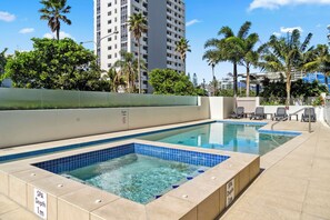A swimming pool area with two separate pools, one labeled SPA Depth 1m and the other 1.8m, surrounded by palm trees and a high-rise building in the background. - Cotton Tree Ocean Views + Romantic Getaway (Maroochydore)