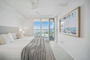A modern bedroom with a large bed, a view of the sea through the window, and a framed picture on the wall. - Cotton Tree Ocean Views +  Romantic Getaway (Maroochydore)