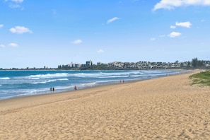 A wide sandy beach with gentle waves and a clear sky.
