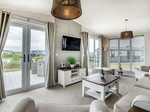 En moderne stue med et fjernsyn, hvide møbler og udsigt til vand og bygninger.