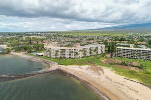 A coastal hotel with multiple buildings, a beach, and a view of the distant landscape. - Menehune 127 Partial Ocean Views in Well Maintained Condo Home (Kihei)