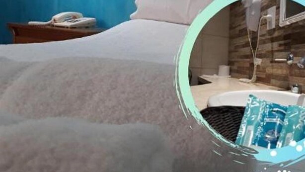 Habitació d'hotel amb llit, una tauleta de nit, una làmpada i una làmpada de paret.