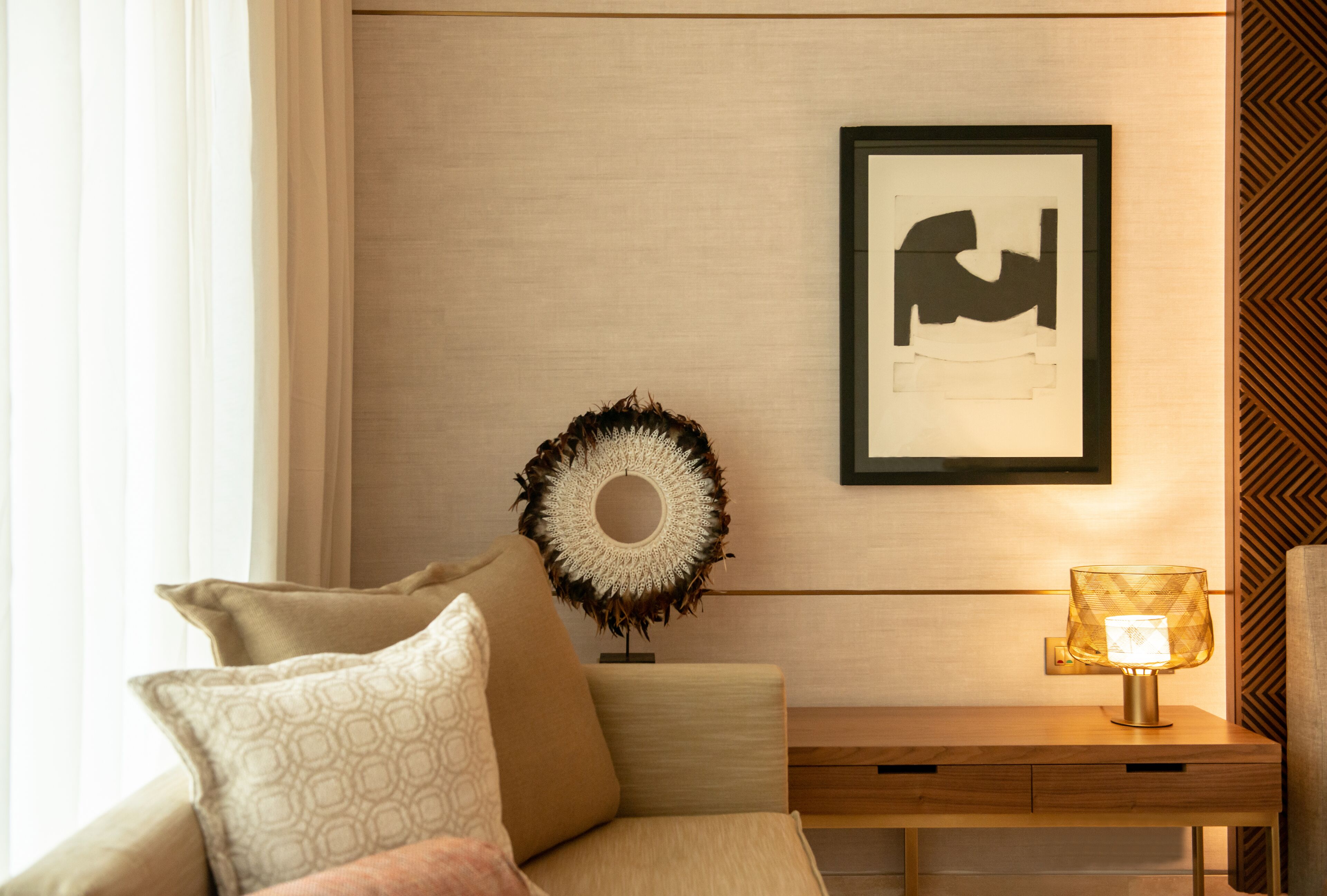 A modern living room with a sofa, a decorative wall piece, a framed artwork, and a table lamp.