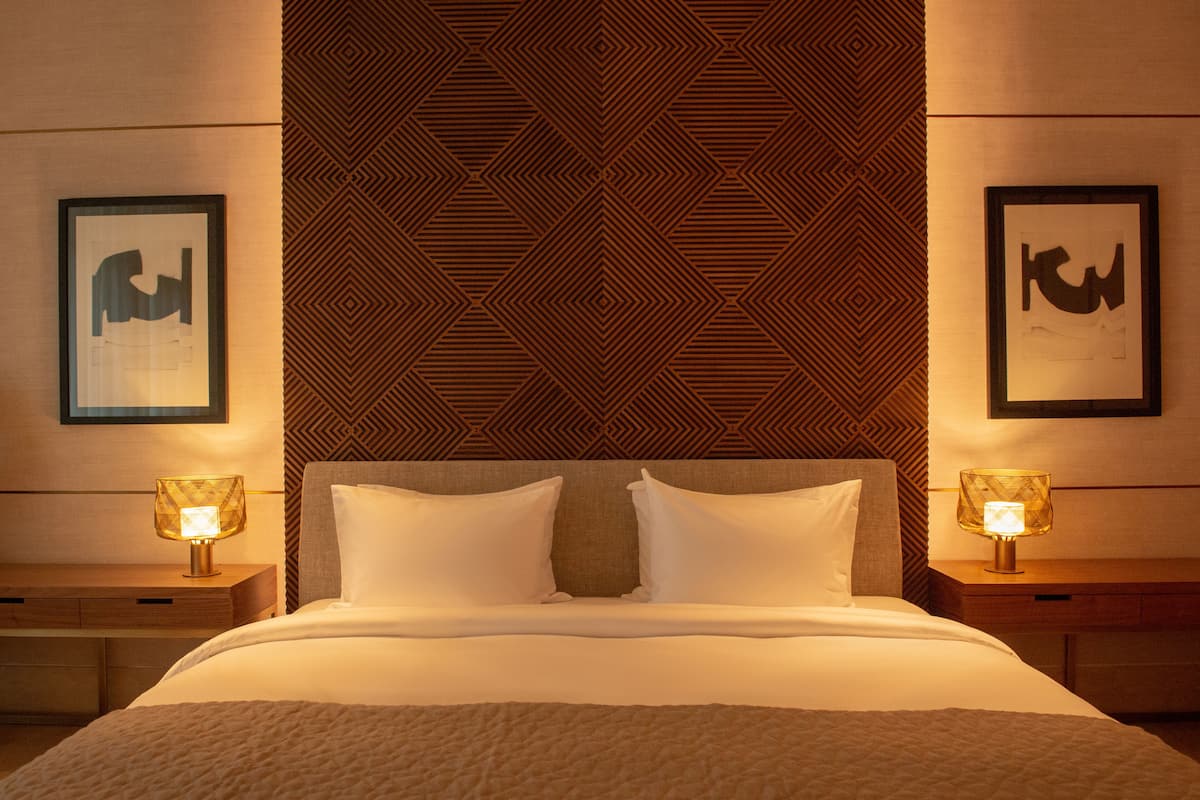 A hotel room with a large bed, two bedside tables with lamps, and a geometric patterned wall.