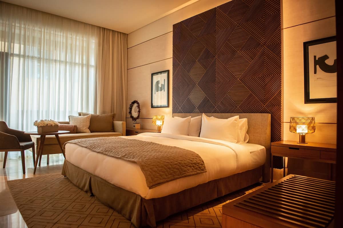 A hotel room with a large bed, a desk, a chair, and a patterned wall.