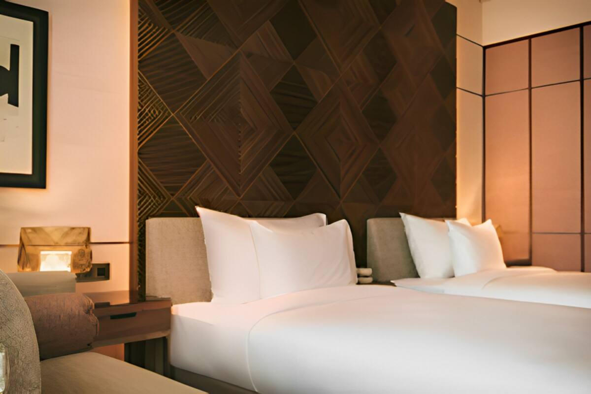A hotel room with two beds, a nightstand, a lamp, and a geometric patterned wall.