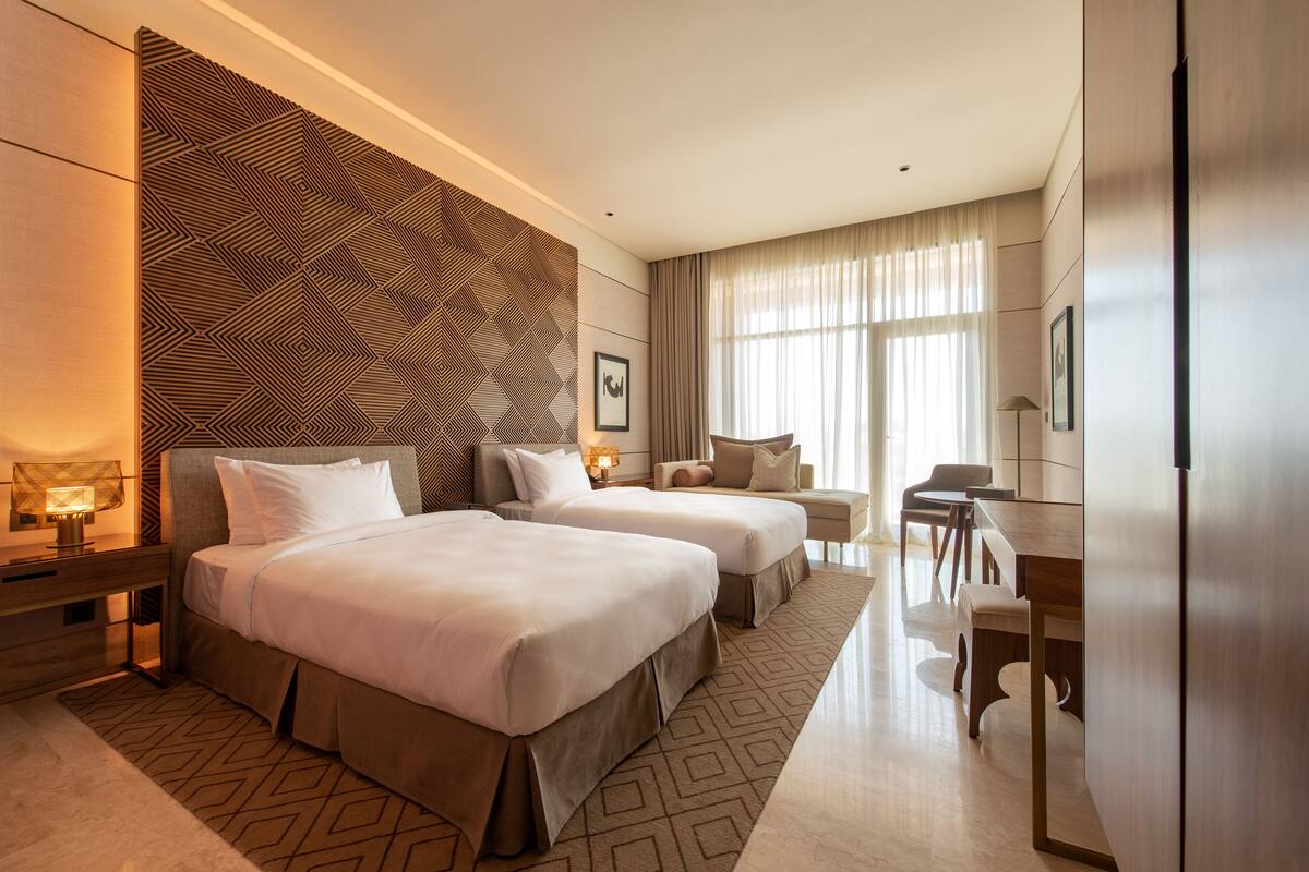 A hotel room with two beds, a desk, and a dining area.