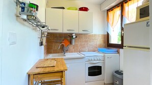 A compact kitchen with white cabinets, a stove, a sink, and a small trash bin.