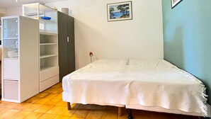 A small room with a bed, a wardrobe, a ceiling fan, and a picture on the wall.