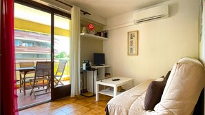 A compact living space with a sofa, a small table, a TV, and a balcony with chairs.