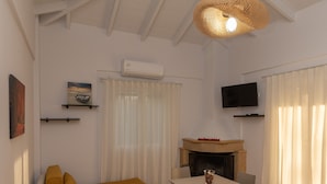 Een moderne woonkamer met een bank, een eettafel, stoelen, een hanglamp, een open haard en een aan de muur bevestigde televisie.