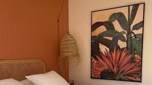 Un dormitorio con cama, almohadas, una lámpara colgante y un cuadro en la pared.