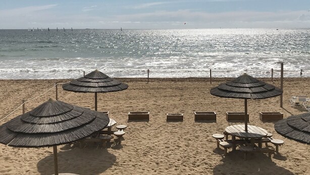 Una playa con varias sombrillas de paja y sillones de madera.