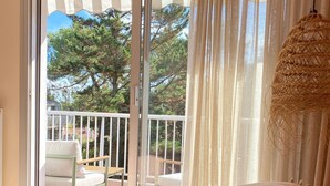 Un dormitorio con una cama grande, un balcón con una silla y vistas a árboles y una casa.