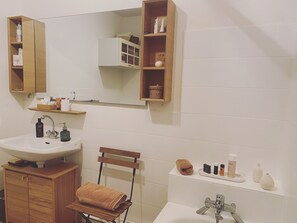 A bathroom with a wooden vanity, a sink, a mirror, and shelves with toiletries.