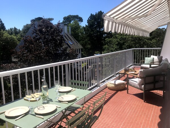 A balcony with a dining table set for four, outdoor furniture, and a white railing.