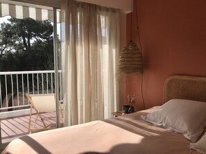 A bedroom with a bed, a hanging light fixture, a window with curtains, and a view of trees outside.