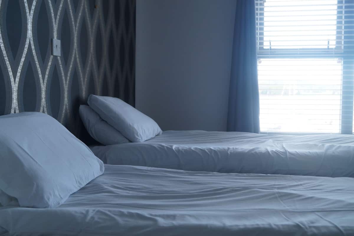 Une chambre d’hôtel avec deux lits, un mur décoré d’un motif et une fenêtre avec des stores.