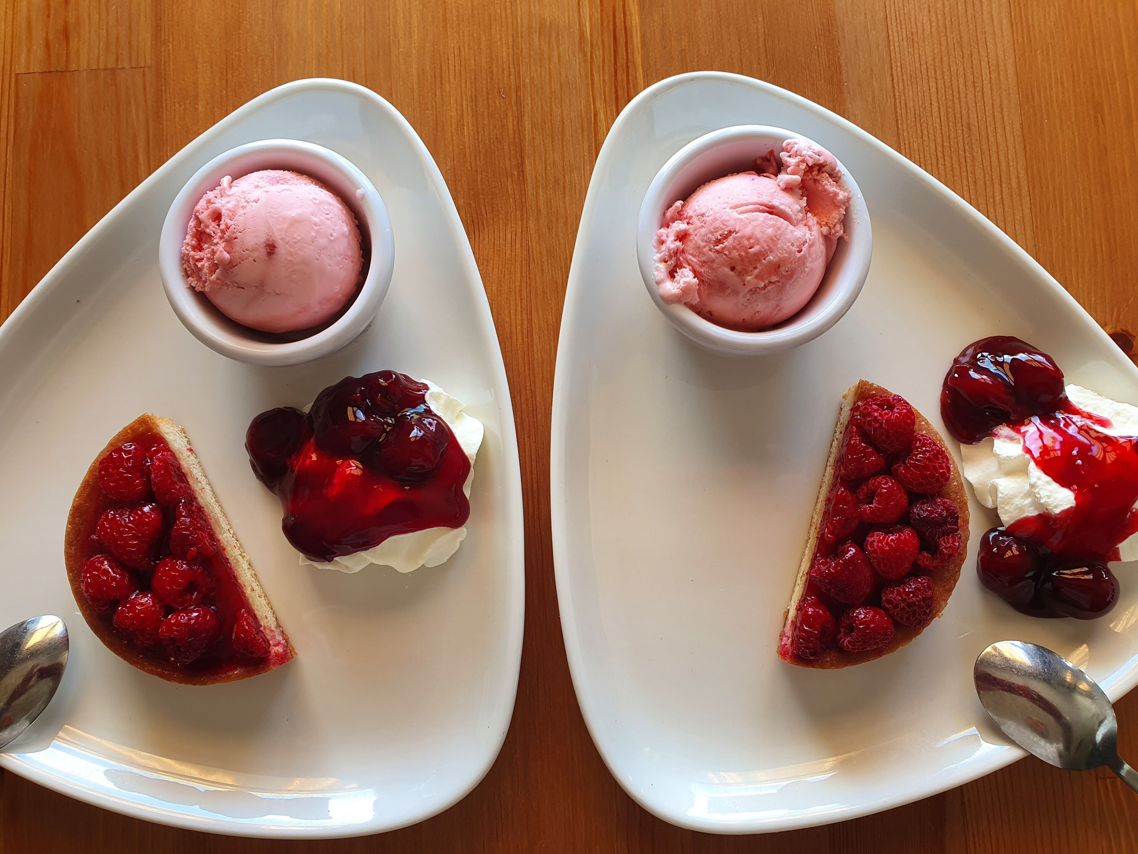 Two white plates with desserts, each containing a slice of cake with raspberry compote and a scoop of pink ice cream.