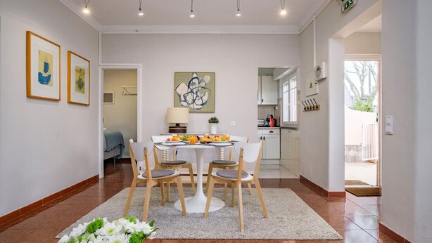 A modern dining area with a round table, white chairs, and a floral centerpiece.