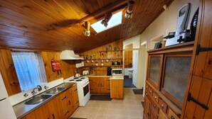 A compact kitchen with wooden cabinets, a stove, and a microwave. - Miss Mabel Cottage · Burra - Historic (Burra)