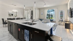 Cocina moderna con isla central, electrodomésticos integrados y comedor con sofá y sillas.