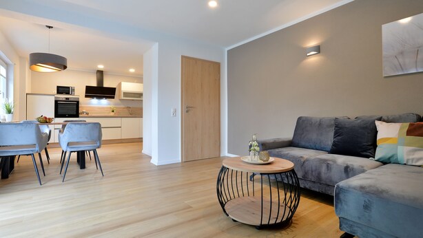 A modern living room with a grey sofa, a round coffee table, and a dining area with a table and chairs.