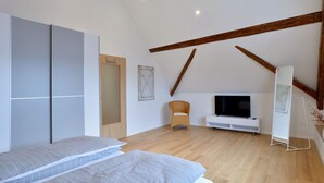 A bedroom with a bed, a television, a wardrobe, and a wooden ceiling beam.