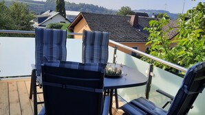 A wooden deck with a table and chairs, overlooking a residential area with houses and wind turbines.